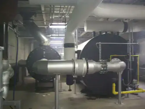Large industrial boiler installation featuring massive black vessels, heavy piping, and support structures.